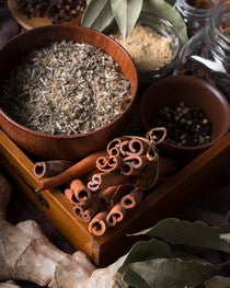 Overview shot of a bowl of grains, cinnamon sticks and other herbs in a wood box. 